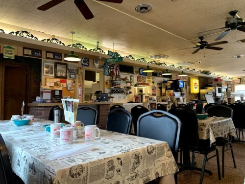 A cozy diner interior with tables covered in newspaper print, a counter with vintage decor, and ceiling fans.