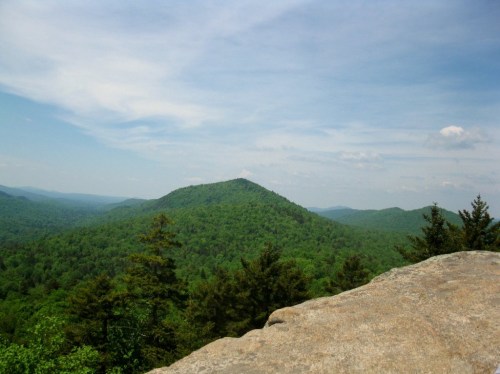A panoramic view of lush green mountains under a blue sky with scattered clouds.