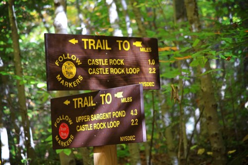Wooden trail signs in a forest, indicating directions and distances to Castle Rock and Upper Sargent Pond.