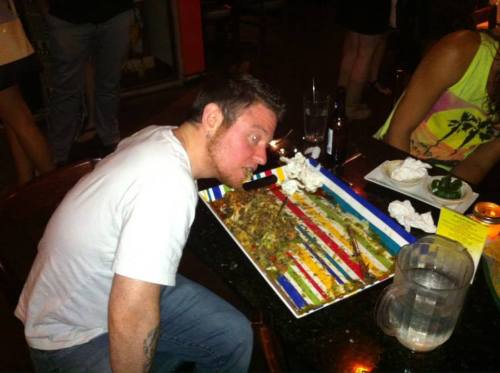 A person leans over a colorful plate of food, preparing to eat, with napkins and drinks on the table.