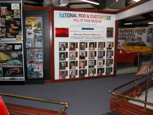 Wall display at the National Rod & Custom Car Hall of Fame Museum featuring photos of board members and museum information.