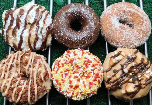 A variety of six donuts with different toppings, including chocolate, sprinkles, and drizzled icing on a green background.