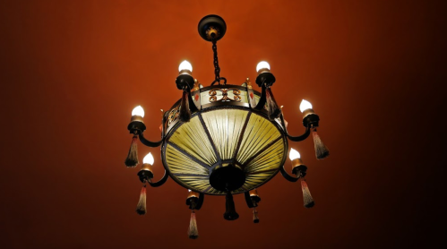 A decorative chandelier with multiple lights hanging from a ceiling against a warm red background.