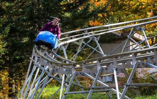 A person rides a blue coaster on a winding track surrounded by colorful autumn trees.