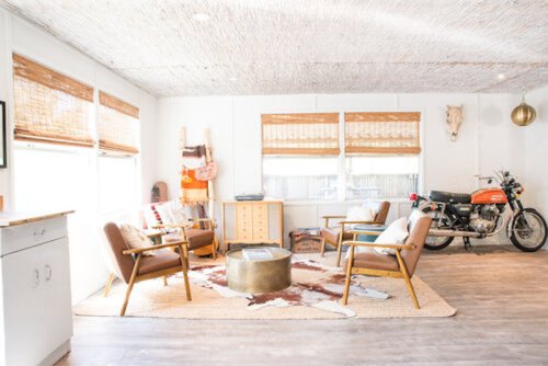 Cozy living room with modern furniture, a round coffee table, and a vintage motorcycle in the corner. Natural light from windows.