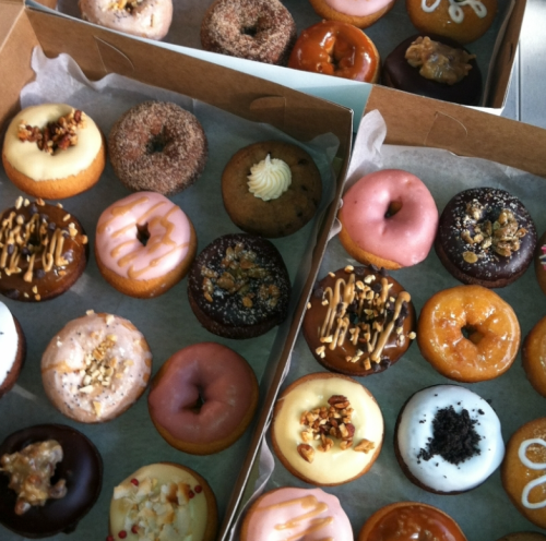 Two boxes filled with a variety of colorful donuts, including glazed, frosted, and topped with sprinkles and nuts.