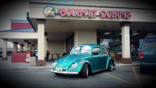 A vintage teal Volkswagen Beetle parked outside a shop named "Country Donuts."