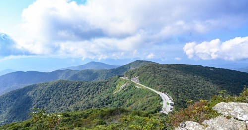 A scenic view of rolling mountains and a winding road under a partly cloudy sky.