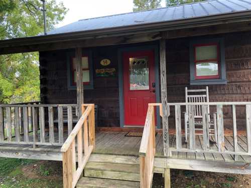 A rustic wooden cabin with a red door and rocking chairs on the porch, surrounded by greenery.