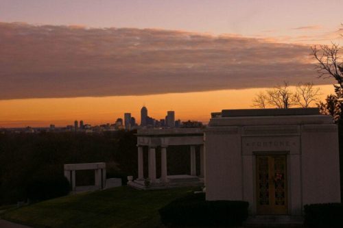 A sunset view over a city skyline, with a cemetery and mausoleums in the foreground.