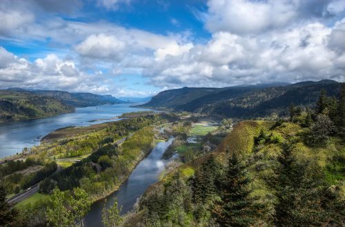 A scenic view of a river winding through lush green hills under a partly cloudy sky.