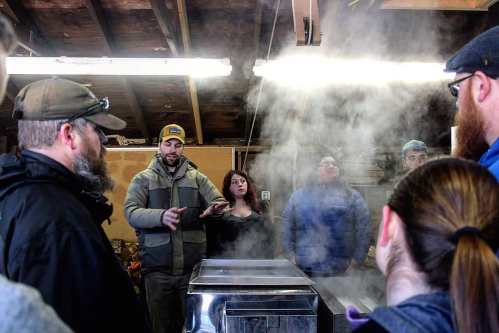 A group of people gathers in a workshop, surrounded by steam, as one person explains a process.