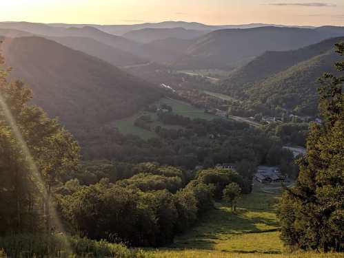 A scenic view of rolling green hills and valleys under a golden sunset, with a winding river in the distance.