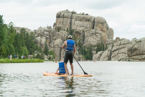 A person paddleboarding on a calm lake, surrounded by rocky cliffs and lush greenery.