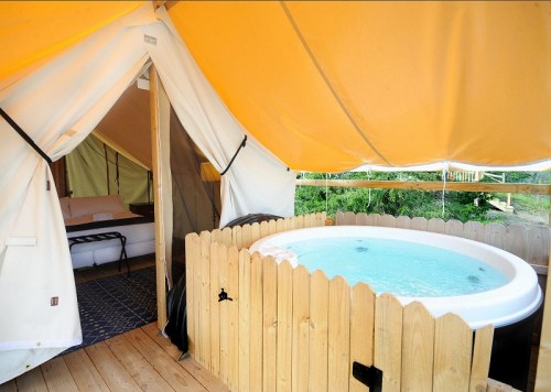A cozy glamping tent with a wooden deck featuring a hot tub and a view of nature.