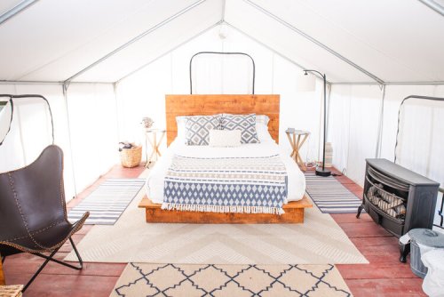 Cozy glamping tent interior featuring a wooden bed, patterned blankets, a chair, and a small heater.