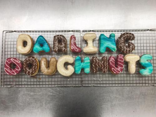 Colorful doughnuts arranged to spell "DARLING DOUGHNUTS" on a wire rack.