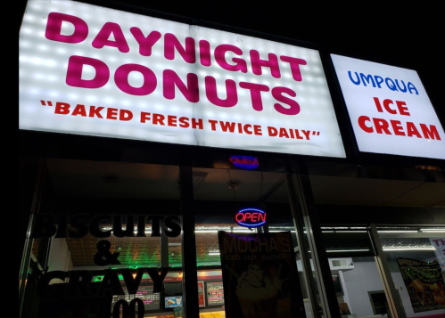 Sign for "Daynight Donuts" and "Umpqua Ice Cream," featuring bright lights and an "Open" neon sign.