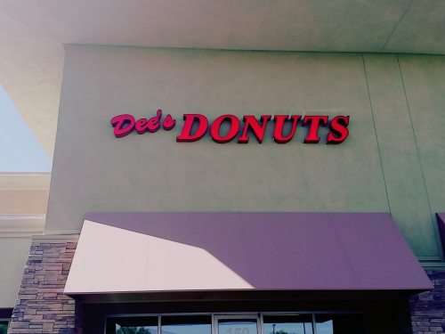 Sign for Dee's Donuts on a storefront, featuring bold red letters against a light background.