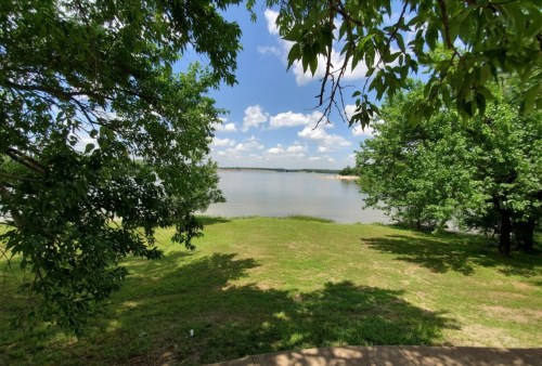 A serene lakeside view framed by green trees and a clear blue sky with fluffy clouds.