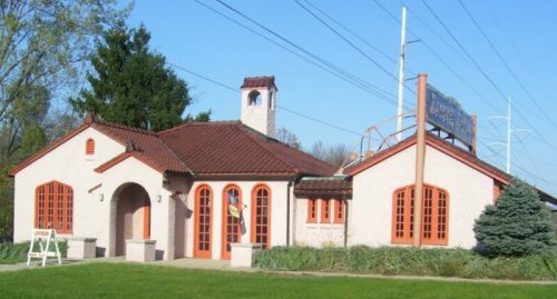 A charming building with a red-tiled roof, orange accents, and large windows, surrounded by greenery and power lines.