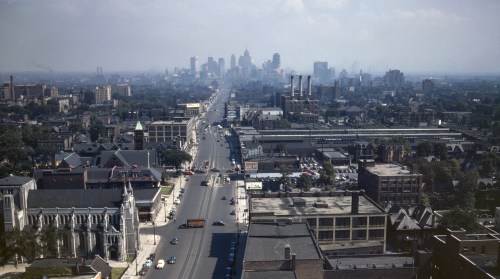 Aerial view of a city skyline with buildings, roads, and industrial areas under a hazy sky.