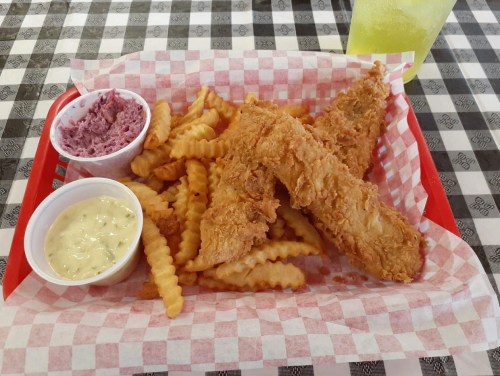 A red tray with crinkle-cut fries, two fried fish fillets, and dipping sauces on a checkered tablecloth.