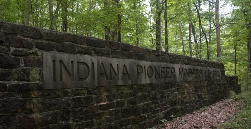 Stone wall with the inscription "Indiana Pioneer Mothers Memorial" surrounded by lush green trees.