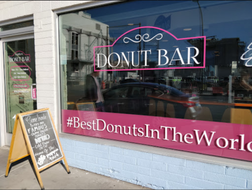 A storefront window displaying "DONUT BAR" and a sign promoting their famous donuts with a hashtag.
