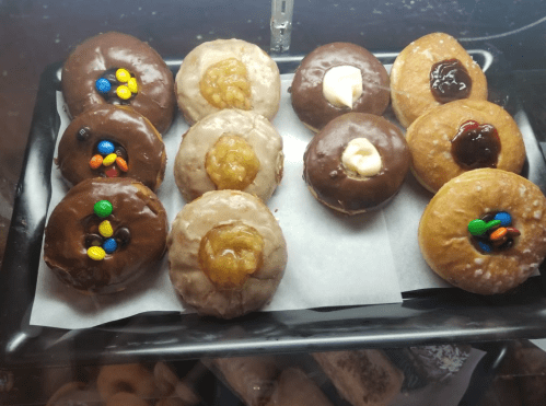 A tray of assorted donuts, including chocolate-covered, glazed, and filled varieties, with colorful toppings.