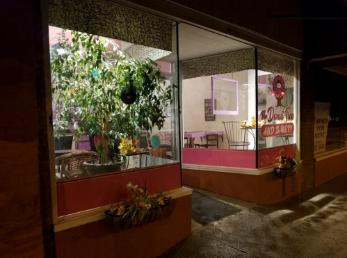 A cozy bakery storefront with large windows, plants, and colorful decor, inviting customers inside.