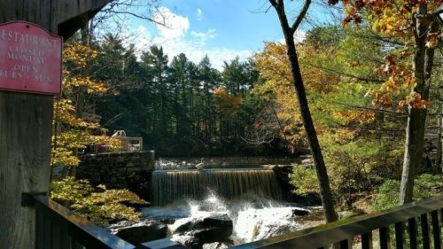 A scenic view of a waterfall surrounded by autumn foliage, with a restaurant sign in the foreground.