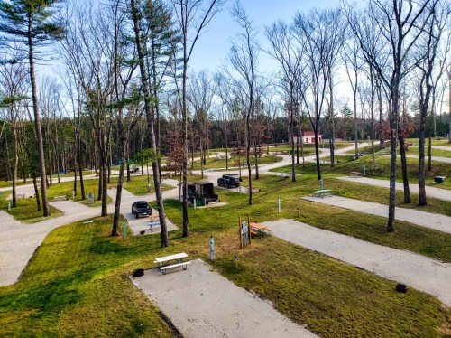 Aerial view of a campground with empty parking spots, surrounded by trees and grassy areas.