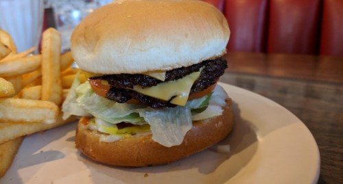 A close-up of a cheeseburger with lettuce, tomato, and a side of golden French fries on a plate.
