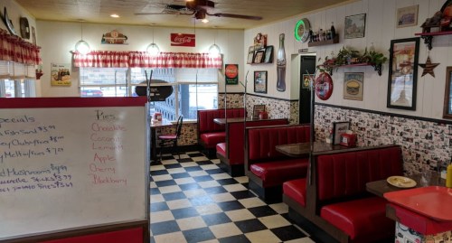 A cozy diner interior with red booths, checkered floor, vintage decor, and a specials board.
