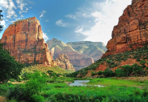A scenic view of Zion National Park featuring towering red rock formations and a lush green valley with a river.