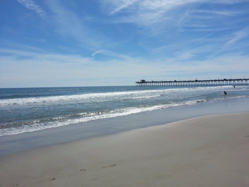 A serene beach scene with gentle waves, a clear blue sky, and a pier in the distance.