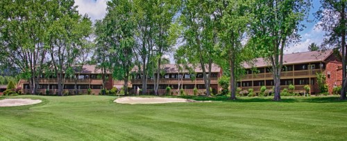 A brick building with multiple balconies surrounded by lush green trees and a golf course with sand traps in the foreground.