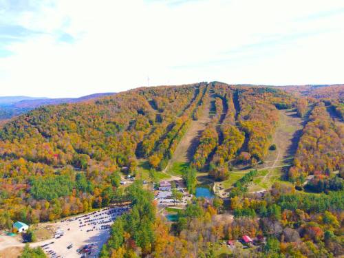 Aerial view of a colorful autumn landscape with a ski slope, parking area, and surrounding trees.