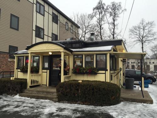 A cozy, yellow diner with snow on the ground, surrounded by greenery and a few people outside.
