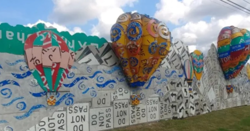 Colorful mural featuring hot air balloons and whimsical designs on a fence, with blue skies and clouds in the background.