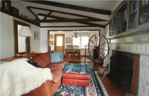 Cozy living room with a brown sofa, wooden dining table, and rustic decor, featuring exposed beams and a fireplace.