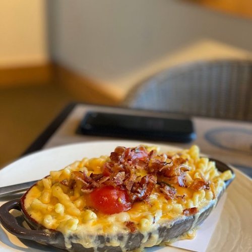 A serving of macaroni and cheese topped with bacon and a cherry tomato, served in a skillet on a plate.