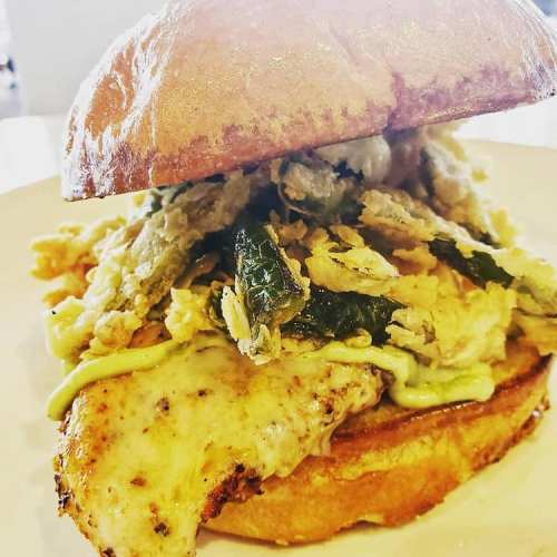 A close-up of a chicken sandwich topped with crispy greens and sauce, served on a toasted bun.