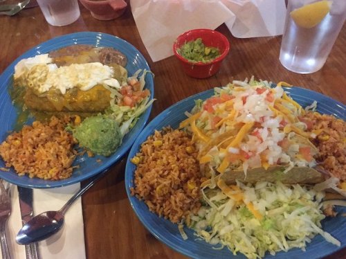Two colorful plates of Mexican food featuring enchiladas, tacos, rice, guacamole, and fresh toppings.