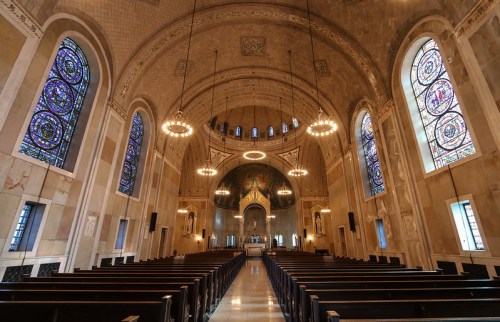 Interior of a grand church featuring stained glass windows, wooden pews, and a beautifully arched ceiling.