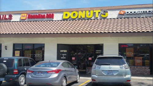 A storefront with a sign reading "DONUTS," featuring parked cars and an "OPEN" sign.