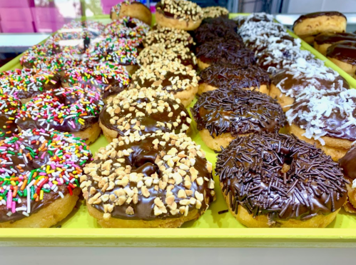 A colorful assortment of donuts topped with chocolate, sprinkles, nuts, and coconut, displayed on a yellow tray.
