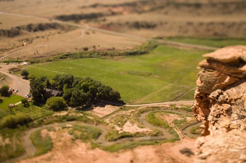 Aerial view of a green landscape with winding rivers and a small house, surrounded by rocky terrain and open fields.