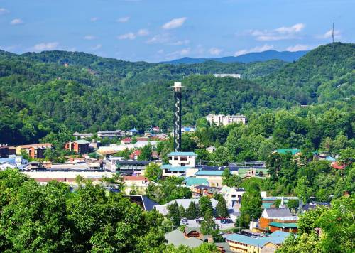 A scenic view of a small town surrounded by lush green mountains, featuring a tall observation tower.